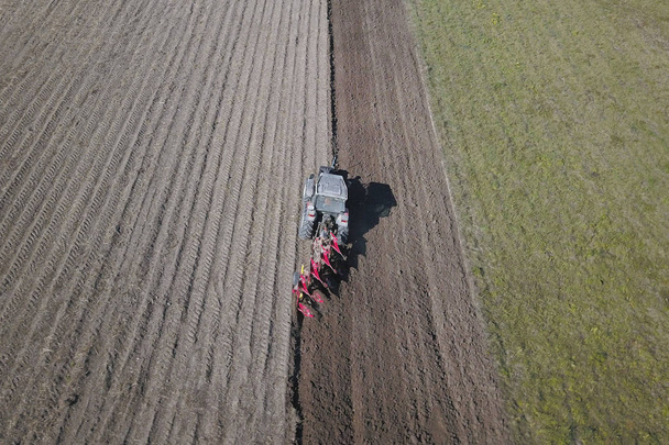 Фермер на червоному тракторі з сіячем сіє зерно в оранці землі в приватному полі в селі. Механізація весняно-польових робіт. Повсякденне життя фермера. Переробка землі. Аграрний
. - Фото, зображення