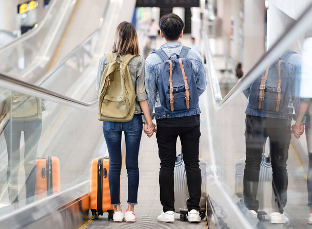 Happy loving Asian couple traveling with baggage getting down on the escalator to the departure area at the airport. Lover travel and transportation concept. - Zdjęcie, obraz