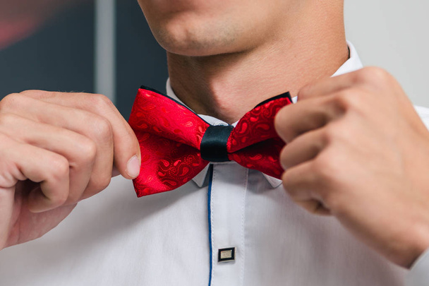 A man in a white shirt ties a red bow tie while preparing for a wedding ceremony close up - Foto, afbeelding