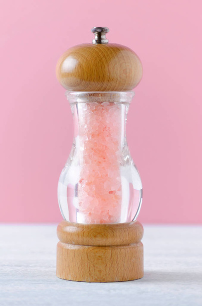 růžová himálajská sůl krystaly v sklo dřevěný mlýnek na růžovém pozadí - Fotografie, Obrázek
