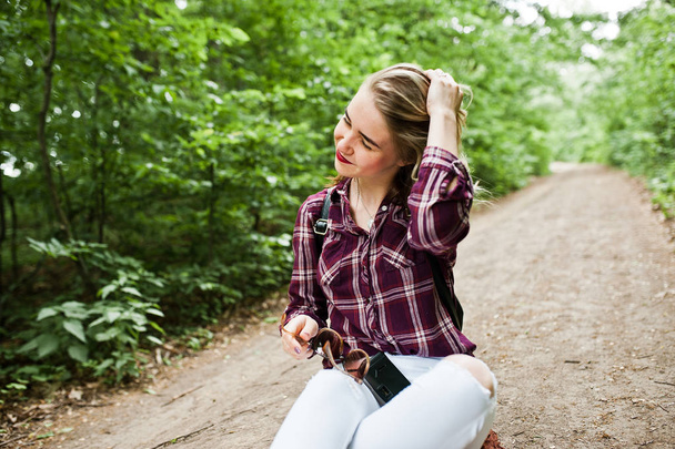 Portrait of a beautiful blond girl in tartan shirt sitting on the ground in the countryside. - Photo, image