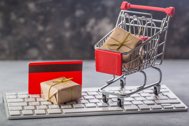 Christmas or New year gift paper box gold ribbon in a small shopping cart on a laptop keyboard. Concepts about online.e-commerce or electronic commerce is a transaction of buying or selling at home - Fotó, kép