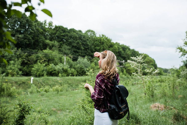 田舎を歩いてバックパックでタータン チェック シャツで魅力的なブロンドの女の子の肖像画. - 写真・画像
