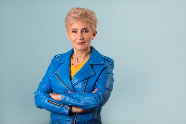 stylish woman at the age with a short hairstyle in a blue jacket on a blue background - Фото, зображення