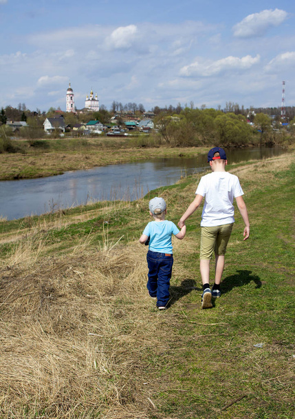 Two little boys walking on the river bank on horizon line background. Brothers holding hands and walking by the field. - Фото, зображення