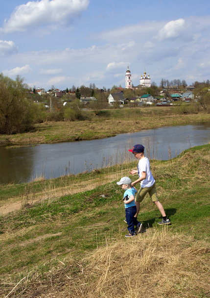 Twee kleine jongens lopen op de rivier bank op horizon lijn achtergrond. Broers hand in hand en wandelen door het gebied. - Foto, afbeelding