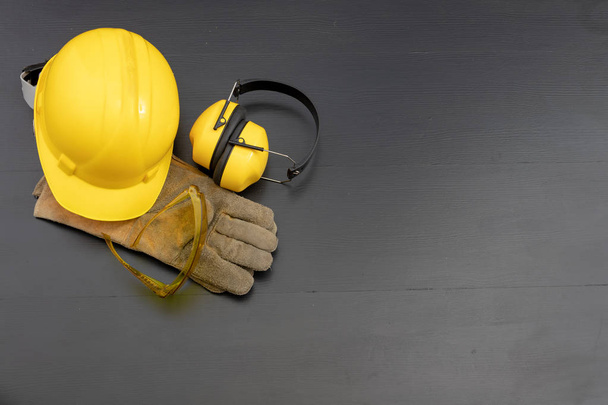Helmet and gloves on a black workbench. Work clothing for construction workers. Dark background. - Fotoğraf, Görsel