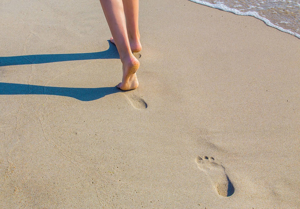 τα πόδια ενός κοριτσιού με τα πόδια σε μια αμμώδη παραλία κατά μήκος την άκρη του νερού - Φωτογραφία, εικόνα