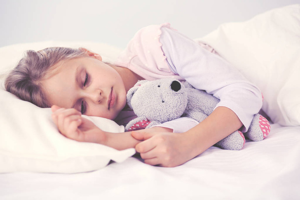 Child little girl sleeps in the bed with a toy teddy bear. - Foto, imagen
