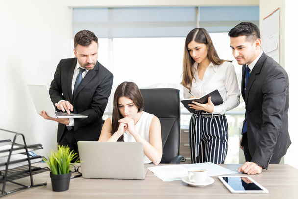 Pracy kobieta z kolegami, patrząc na laptopa podczas spotkania w biurze - Zdjęcie, obraz