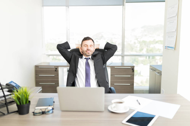 Relajado abogado masculino con las manos detrás de la cabeza sentado en el escritorio en la oficina
 - Foto, imagen