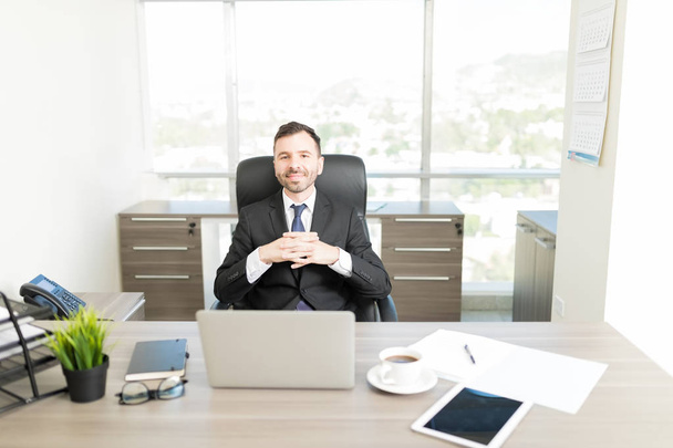 オフィスのデスクで握りしめられる手に座っているハンサムな企業マネージャーの肖像画 - 写真・画像