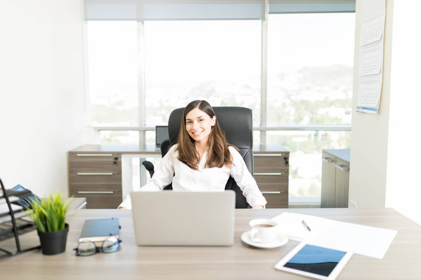 Портрет усміхненої жінки-фінансового радника, що сидить за столом в офісі
 - Фото, зображення