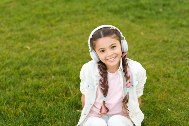 Girl with headphones nature background. Positive influence of music. Child girl enjoying music modern earphones. Childhood and teenage music taste. Little girl listening music enjoy favorite song - Fotó, kép