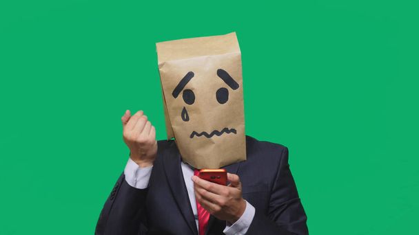 concept van emotie, gebaren. een man met een pakket op zijn hoofd, met een geschilderde smiley huilen, triest, praten aan de telefoon - Foto, afbeelding