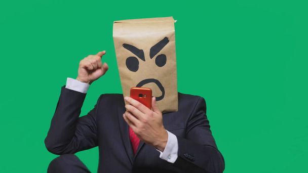 concept van emotie, gebaren. een man met een pakket op zijn hoofd, met een geschilderde smiley agressief en boos. praten op een mobiele telefoon - Foto, afbeelding