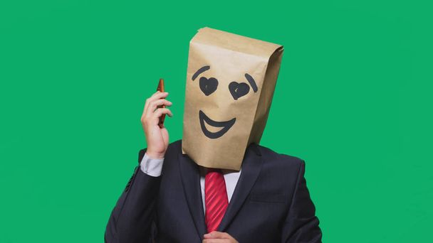 concept of emotions, gestures. a man with paper bags on his head, with a painted emoticon, smile, joy, love. talking on a cell phone - Photo, Image