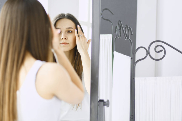 Young woman looking herself reflection in mirror at home. - Foto, Imagen