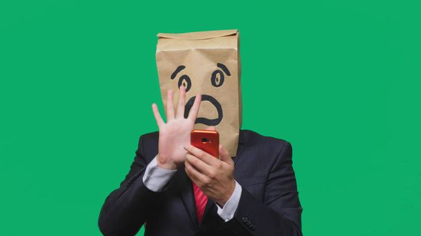 concepto de emociones, gestos. un hombre con bolsas de papel en la cabeza, con un emoticono pintado, miedo. hablando por un teléfono celular
 - Foto, Imagen