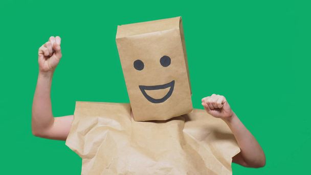 concept van emoties, gebaren. een man met papieren zakken op zijn hoofd, met een geschilderde emoticon, glimlach, vreugde - Foto, afbeelding