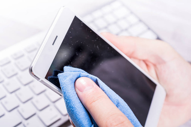 Καθαρισμός ένα Smartphone οθόνη από σκόνη, βρωμιά και τα δακτυλικά αποτυπώματα με ένα καθαρισμό σκουπίστε στο γραφείο του επιχειρηματία - Φωτογραφία, εικόνα