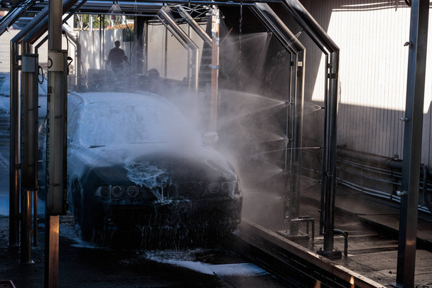 Car being spray washed in an automated car wash, Car being spray washed in a automated car wash, workers in background - Photo, Image