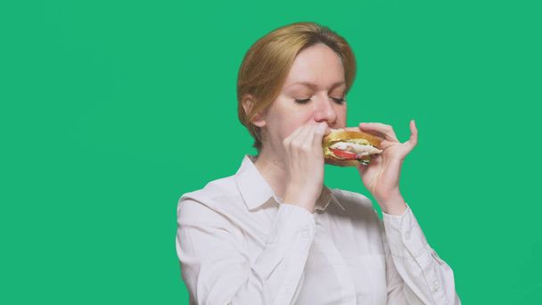 business woman eating a sandwich on a green background. quick lunch concept. - Zdjęcie, obraz