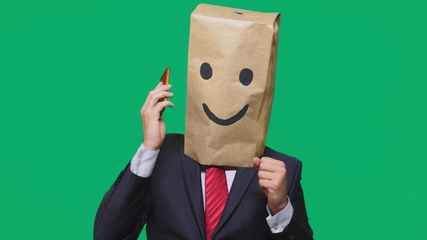 concept of emotions, gestures. a man with paper bags on his head, with a painted emoticon, smile, joy. talking on a cell phone - Photo, Image