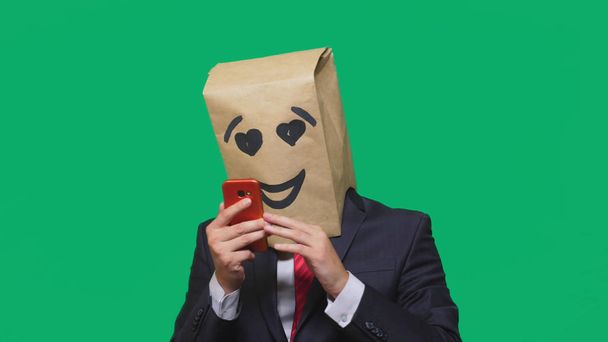 concept of emotions, gestures. a man with paper bags on his head, with a painted emoticon, smile, joy, love. talking on a cell phone - Foto, afbeelding