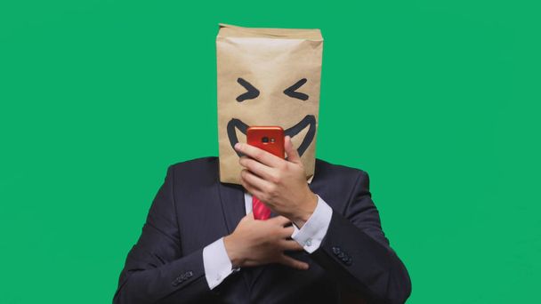 concept of emotions, gestures. a man with paper bags on his head, with a painted emoticon, smile, joy. talking on a cell phone - Photo, Image