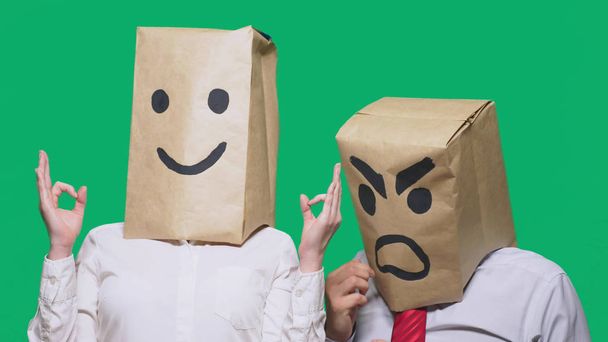 El concepto de emociones y gestos. Dos personas en bolsas de papel en la cabeza con emoticonos pintados. Sonriente agresivo jura. La segunda le sonríe
. - Foto, Imagen