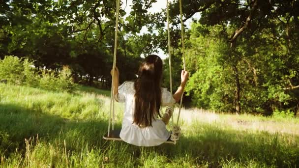 dívka s dlouhými vlasy v bílých šatech, houpání na houpačce v letním parku. Zpomalený pohyb. - Záběry, video