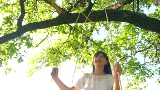 Dziewczyna jest jazda na huśtawce w parku miejskim i uśmiechając się w blasku słońca - Materiał filmowy, wideo