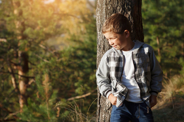 Хлопчик-підліток у плетеній сорочці біля дерева в хвойному осінньому лісі
. - Фото, зображення