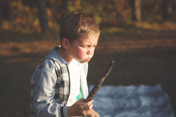 Boy blows on a smoldering branch in the autumn forest. - Photo, Image