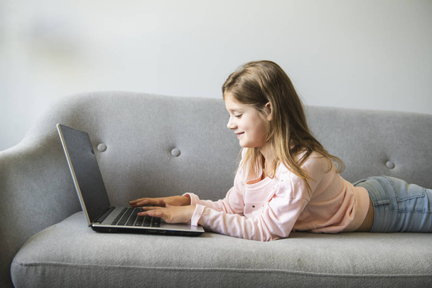 Little girl surfs on the internet lay on the sofa - Фото, зображення