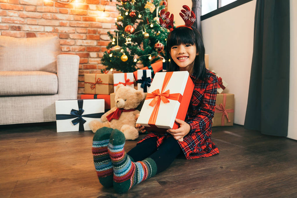 lovely daughter with colorful green socks holding christmas present with red ribbon. Happy little smiling girl with Christmas gift box. Happy Christmas - Kid with gift from santa. - Φωτογραφία, εικόνα