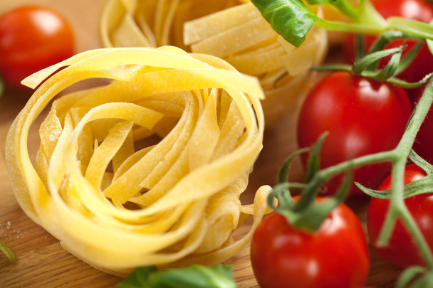 Tagliatelle pasta with fresh basil and tomatoes on rustic table - Фото, зображення