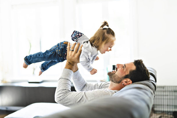 Young father with baby daughter on sofa at home - 写真・画像
