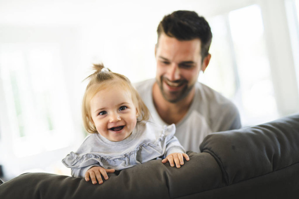 Young father with baby daughter on sofa at home - Foto, Bild