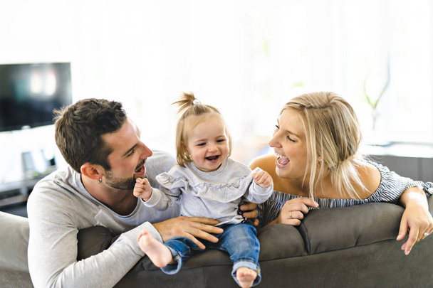 Young family with baby daughter on sofa at home - Φωτογραφία, εικόνα