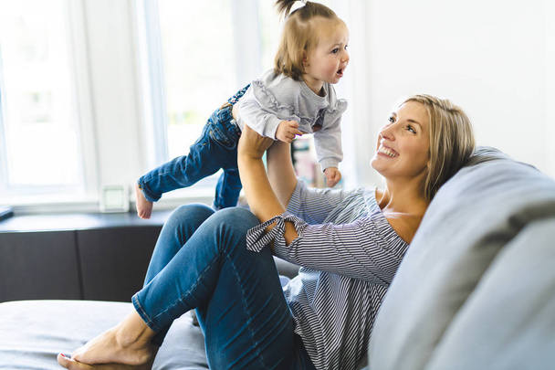 Young mother with baby daughter on sofa at home - Foto, Bild