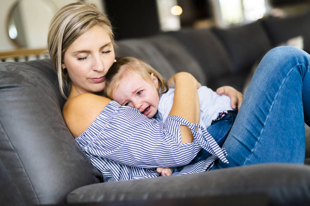 Young mother with baby daughter on sofa at home, the baby crying - Fotografie, Obrázek