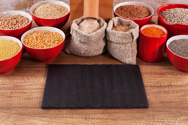 Verschillende granen en zaden rond een tafelblad molen - hele voedsel en gevarieerde voeding concept, kopiëren ruimte - Foto, afbeelding