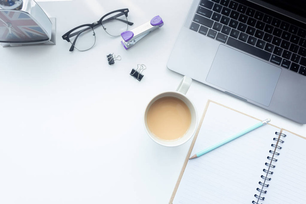 Верхний вид рабочего пространства, ноутбук на белом столе с чашкой кофе и офисное оборудование на заднем плане
 - Фото, изображение