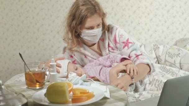 Menina doente com uma temperatura. Criança com febre está deitada na cama com a mãe, comendo frutas e usando um laptop
. - Filmagem, Vídeo