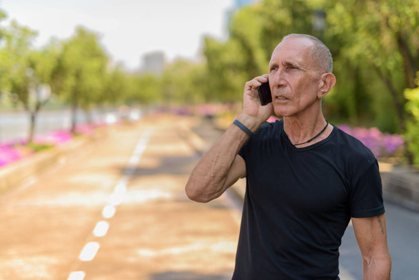 Thoughtful bald senior tourist man talking on mobile phone on th - Photo, Image
