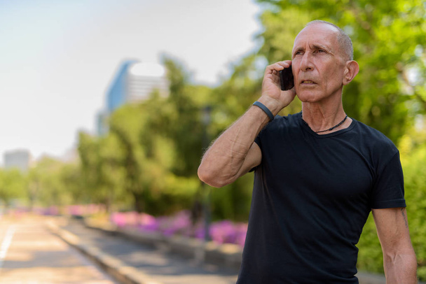 Bald senior tourist man thinking while talking on mobile phone a - Photo, Image