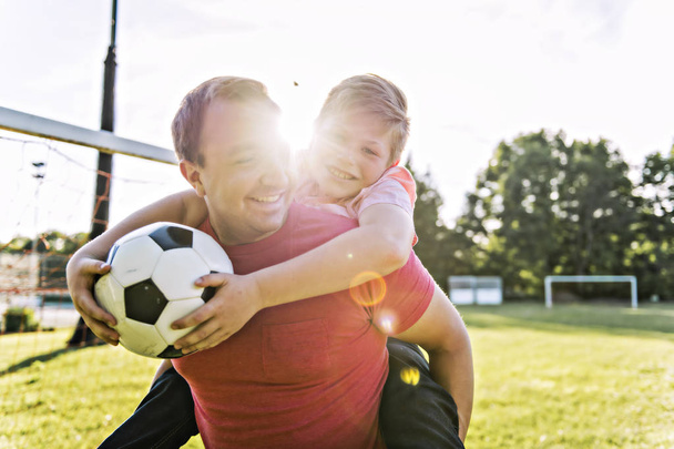 man with child playing football outside on field - Photo, image