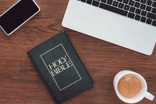 Ansicht der Heiligen Bibel mit neuem Testament, Gadgets und Kaffee auf Holzoberfläche - Foto, Bild